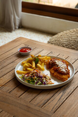 A plate of chicken parmesan or chicken parmigiana, served alongside french fries and salad. On a rustic wooden table, in cafe environment