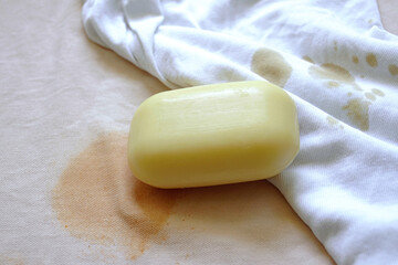 A bar of soap lying on stained fabrics - close-up photo. Removing stains from light-colored knitwear: home washing of white and peach-colored clothing items with ketchup and coffee stains.