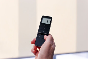Remote control for window blinds. Man holds in his hand black remote control panel with display and...