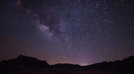 A dramatic night sky filled with stars over a quiet desert landscape.