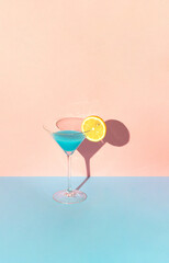 Creative party concept a glass of blue cocktail and a piece of lemon. Summer idea on pink and blue background.