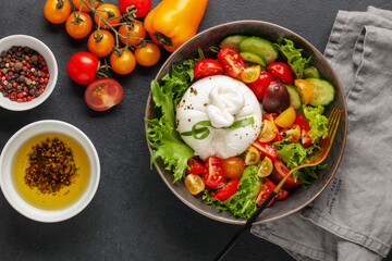 Salad with traditional italian burrata cheese. Burrata ball with cherry tomatoes, cucumber slices, lettuce  and peppercorn in bowl on the table. Top view