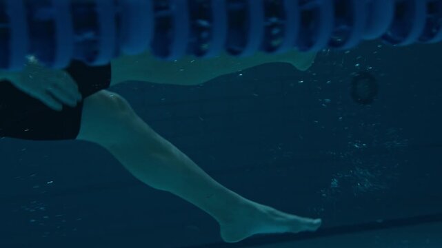 Legs of unrecognizable male swimmer doing backstroke swimming technique underwater