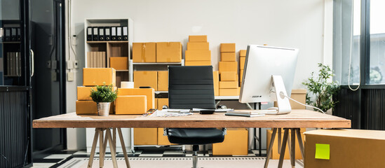 A wooden desk in an SME office, with a laptop, desktop computer, and a parcel cardboard box. The workspace is organized for efficient management, logistics, and order processing.