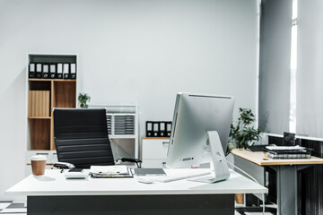 A modern, white-colored business office with a wooden desk, calculator, desktop computer, and a black leather chair. The executive office features private office furniture for the chief of staff.