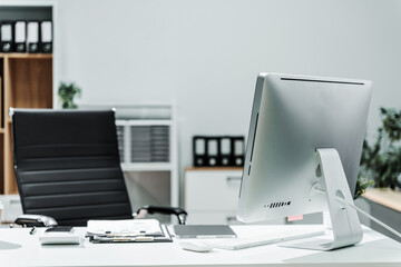 Fototapeta premium A modern, white-colored business office with a wooden desk, calculator, desktop computer, and a black leather chair. The executive office features private office furniture for the chief of staff.