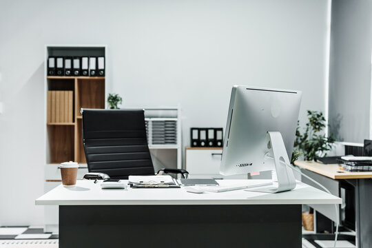 A modern, white-colored business office with a wooden desk, calculator, desktop computer, and a black leather chair. The executive office features private office furniture for the chief of staff.