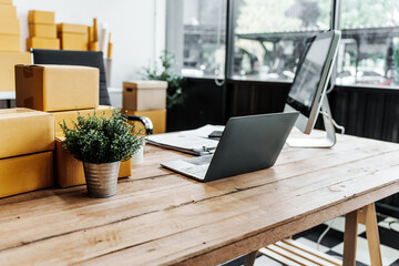 A wooden desk in an SME office, with a laptop, desktop computer, and a parcel cardboard box. The workspace is organized for efficient management, logistics, and order processing.