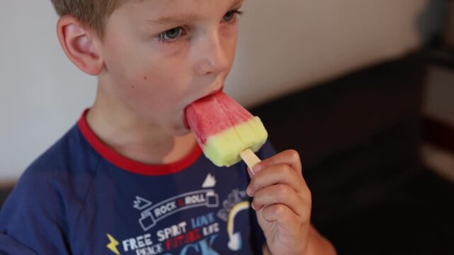 Caucasian Boy Enjoying Colorful Popsicle In Bright Kitchen During Afternoon