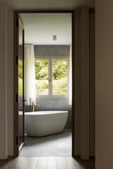 Interior of a modern bathroom with a beautiful bathtub overlooking the green garden of plants