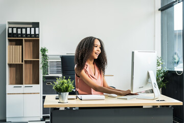 An African American woman with an afro works at a wooden desk in an office, focusing on business...