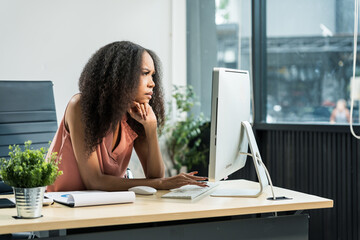 An African American woman with an afro works at a wooden desk in an office, focusing on business...