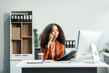 An African American woman with an afro works at a wooden desk in an office, focusing on business...