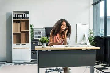 An African American woman with an afro works at a wooden desk in an office, focusing on business...