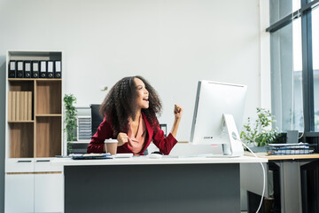 An African American woman with an afro works at a wooden desk in an office, focusing on business...