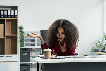 An African American woman with an afro works at a wooden desk in an office, focusing on business...