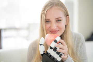 A young woman is using a robotic prosthetic arm attached to her body. She controls her hand to pick...