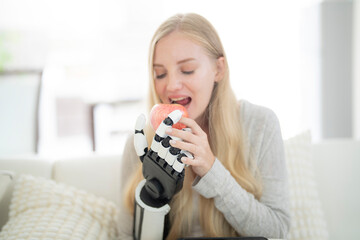 A young woman is using a robotic prosthetic arm attached to her body. She controls her hand to pick...