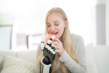 A young woman is using a robotic prosthetic arm attached to her body. She controls her hand to pick...