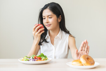 Diet, dieting, happy asian young woman, girl hand push out, deny sweet donut, doughnut on plate, choose red apple and green vegetable salad, eat food for good healthy, female getting weight loss.