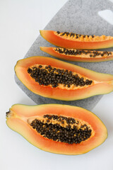 Fresh papaya halves and slices on the grey cutting board on the white background 