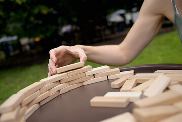 woman pays her attention on playing a wooden block game at a table, moving a wooden block. toy, game, leisure. digital detox