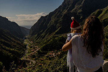 woman holding a child at Christmas on the Scenic mountain landscape with deep green gorge, traditional village, and dramatic peaks under a blue sky Curral das Freiras valley in Madeira, Portuga