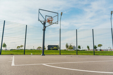 Outdoor basketball court with a metal hoop and fencing, captured under a vibrant, clear blue sky.