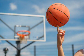 A close-up of a basketball player spinning a ball on their finger, with the hoop blurred in the background.