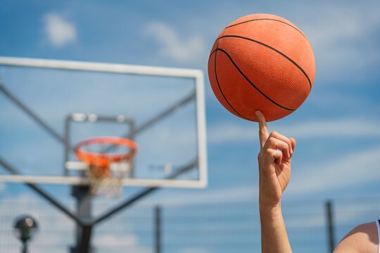 A close-up of a basketball player spinning a ball on their finger, with the hoop blurred in the background.