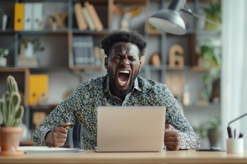 Frustrated Black Man Sitting at Desk in the Office, Expressing Irritation and Anger Over Workplace Stress