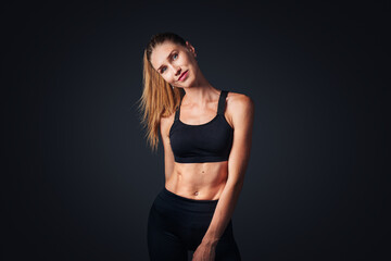 Fototapeta premium Smiling fit woman in fitness outfit isolated on dark background with copy space.