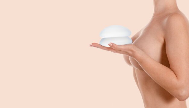 Woman holding implants on hand on beige background. Breast augmentation