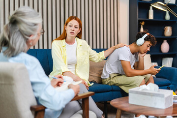 Fototapeta premium Mother comforting sad teenage son during therapy session with psychologist, teenager using earphones