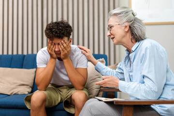 Senior female psychologist comforting sad teenage boy during therapy session