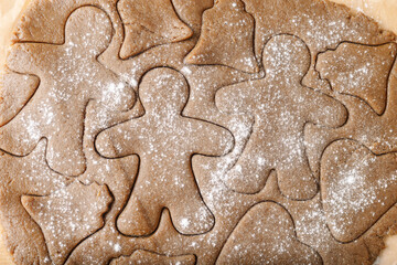 Cooking ginger cookies, Christmas and New Year traditional cookies in shape of gingerbread man, raw rolled out dough with cut out dough figures, closeup texture, top view, pattern on dough, above