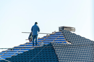 Workers installing metal tile on the roof while roofing house in construction site