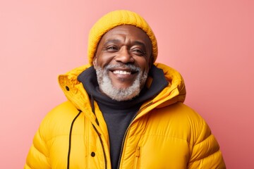 Fototapeta premium Portrait of a cheerful afro-american man in his 60s donning a durable down jacket isolated in pastel yellow background