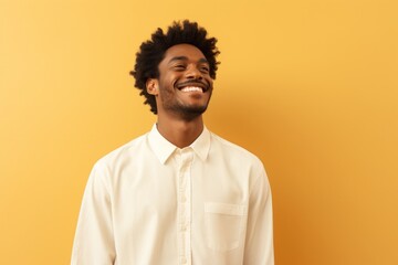 Obraz premium Portrait of a happy afro-american man in his 20s wearing a classic white shirt on pastel yellow background