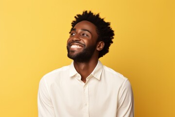 Fototapeta premium Portrait of a happy afro-american man in his 20s wearing a classic white shirt in pastel yellow background