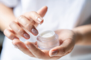 Young woman holding glass jar of cream, closeup