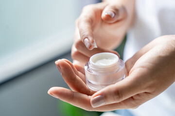 Partial view of woman holding jar with face cream