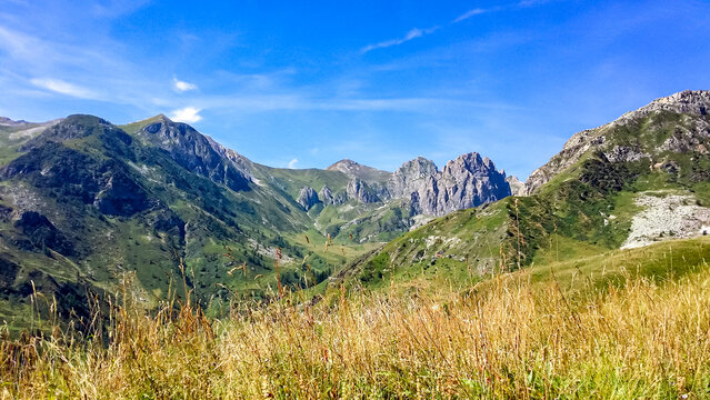 Alpine pasture with panoramic view of mountains and hills in valley Valle Stura in Colle Del Puriac, Piemonte, Italy, Europe. Mtb tour in Italian Alps on sunny summer day. Peaceful serene atmosphere