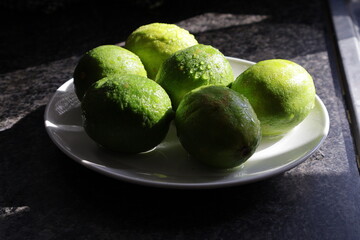 Una toma de cerca de varios limones verdes con agua  en un plato de color blanco en la cocina