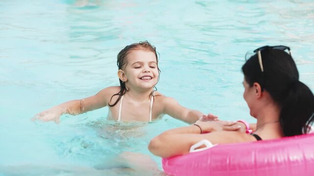 A young woman and her daughter swim in a transparent pool, smile and enjoy the time spent together. The scene captured summer holidays, family happiness, joy and carefree fun, perfect for the holidays