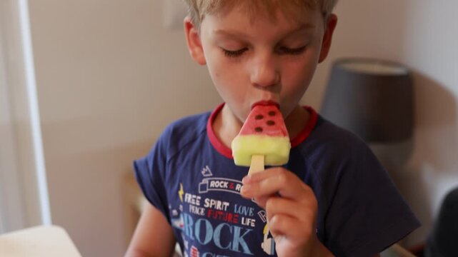 Caucasian Boy Enjoying Watermelon Popsicle While Sitting in Bright Kitchen