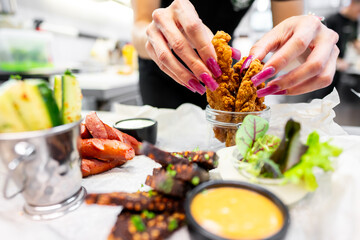 Close-up of hands arranging crispy fried chicken in a glass jar, surrounded by various sauces and side dishes on a kitchen counter. Perfect for food, culinary, and lifestyle themes.