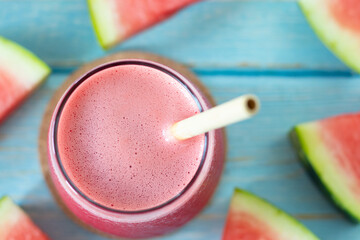 Pink watermelon smoothie with bamboo straw on wooden table with fruit slices. Top view. Close-up....