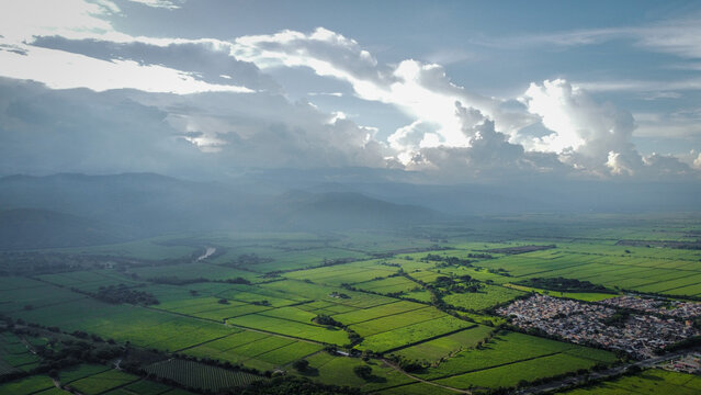 An aerial view of Valle del Cauca, Colombia, featuring lush green fields and distant mountains under dramatic clouds. Perfect for showcasing the natural beauty and agricultural richness of the region.