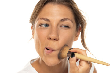 Portrait of a beautiful young woman applying makeup foundation and making faces on a white background